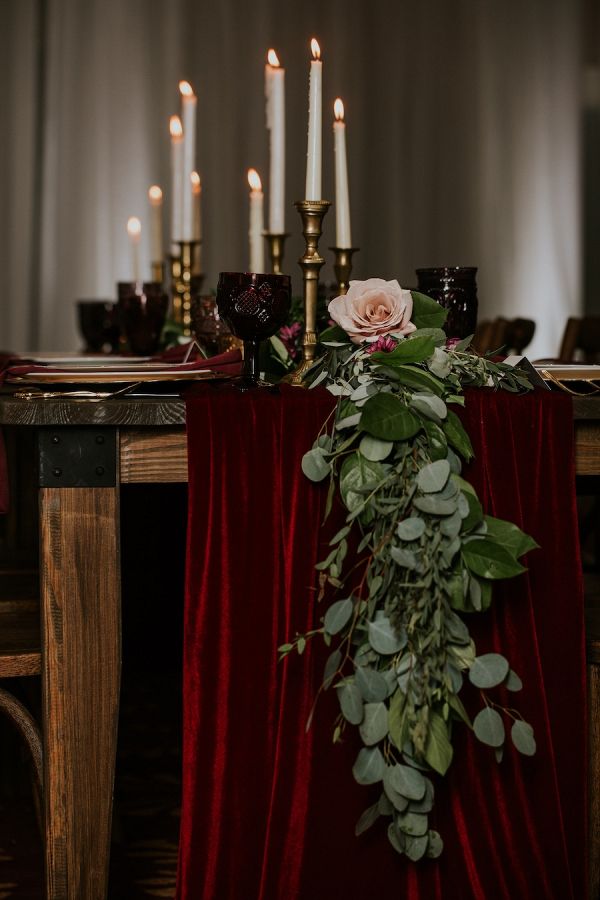 the table is set with candles and greenery for an elegant wedding reception in burgundy velvet