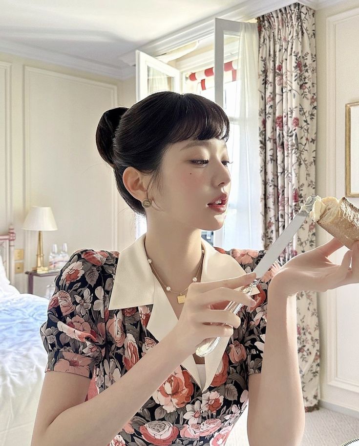 a woman in a floral dress is holding a knife and fork while looking at a piece of food