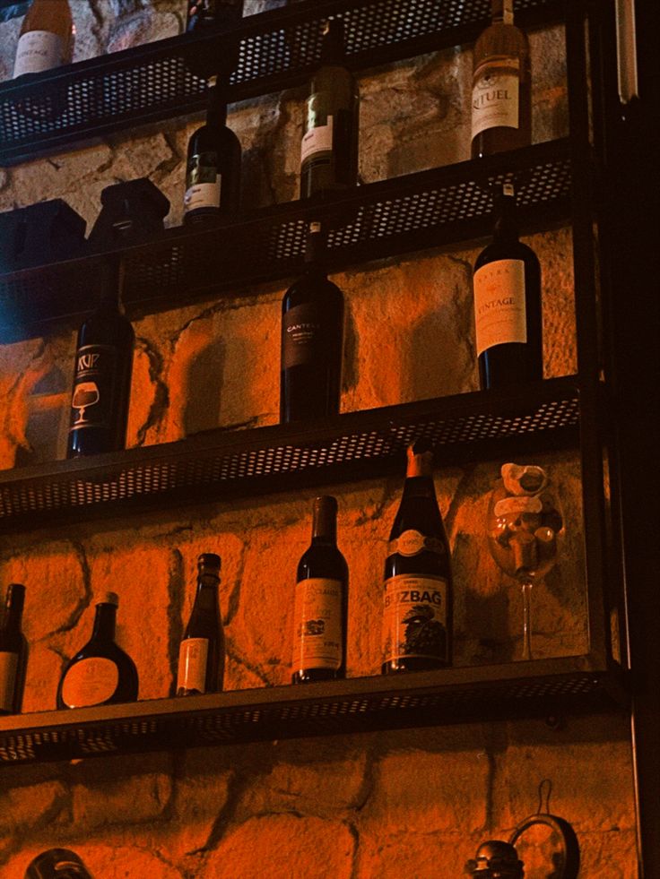 bottles and glasses are on the shelves in front of a brick wall with an orange glow