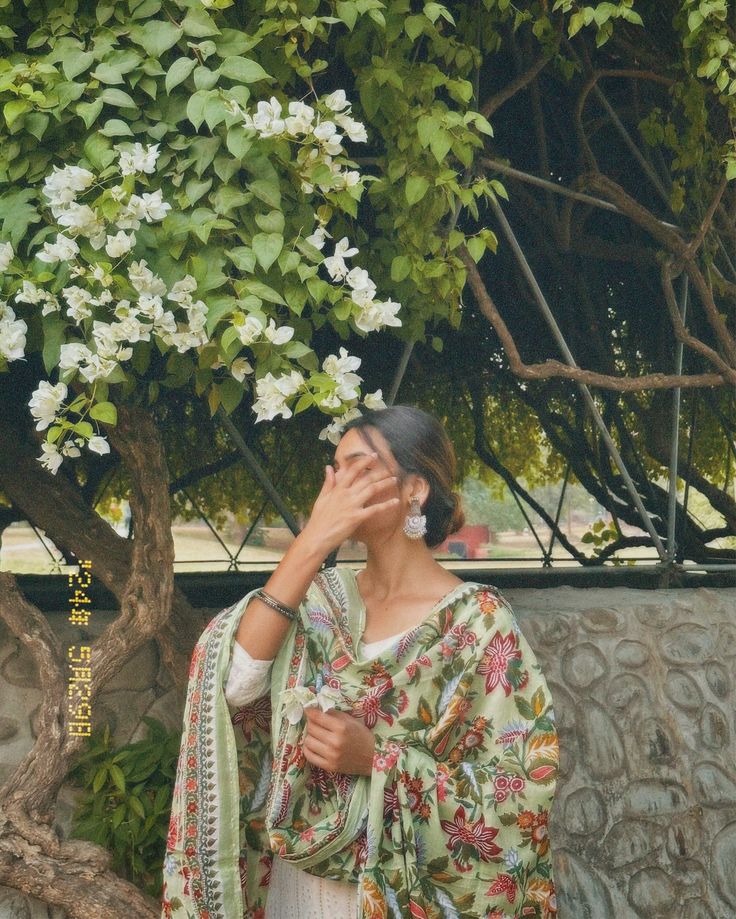 a woman standing in front of a tree with her hands on her face and eyes closed