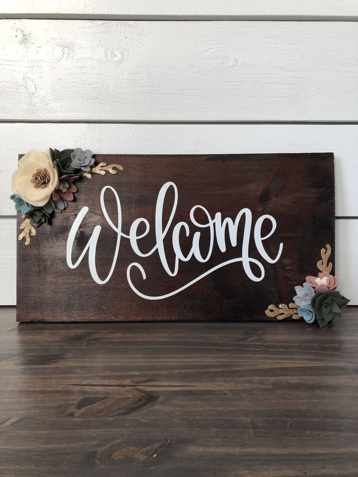 a wooden sign that says welcome with flowers on it and the word welcome written in white