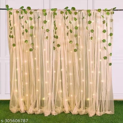 the curtain is decorated with lights and greenery on it's sides, along with green leaves