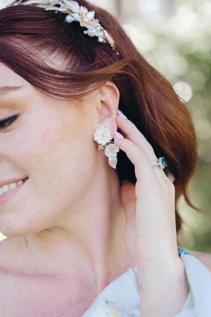 a woman with red hair wearing a white dress and holding her ear to the side