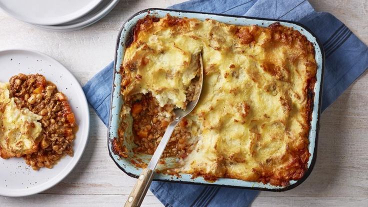 a casserole dish with meat and cheese in it on a blue napkin next to a white plate