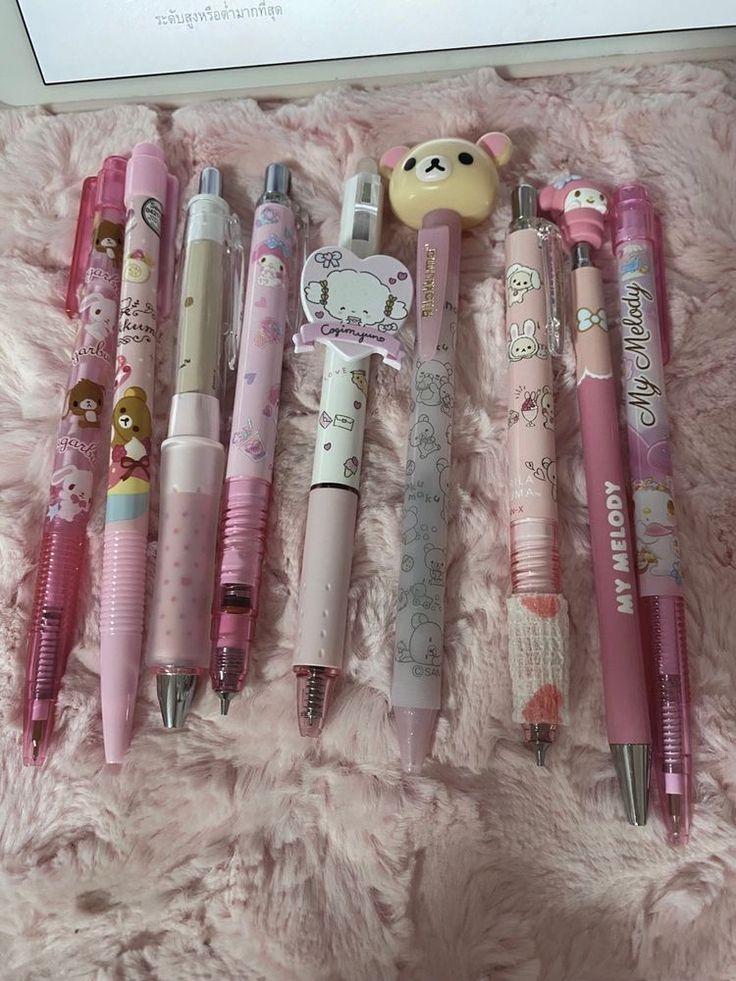 many different pens are lined up on a pink blanket with teddy bears and other items