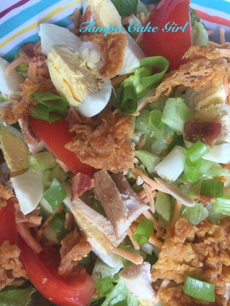 a salad with chicken, lettuce and tomatoes in it on a blue and white plate