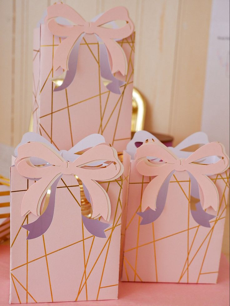 three pink boxes with bows on them sitting on a table next to plates and forks