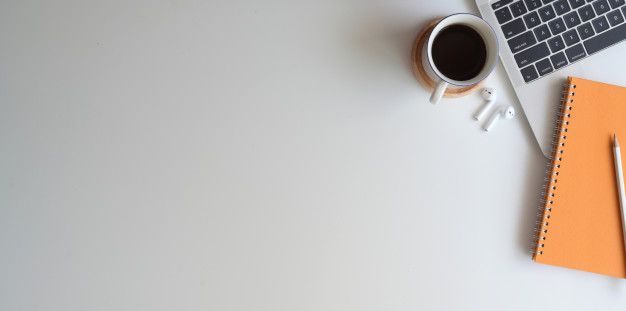 an orange notebook, keyboard and cup of coffee on a white desk with a laptop