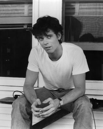 black and white photograph of a young man sitting on the porch with his hands in his pockets