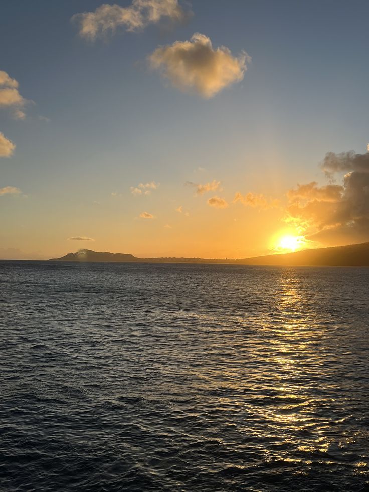 the sun is setting over the ocean with mountains in the distance and clouds in the sky