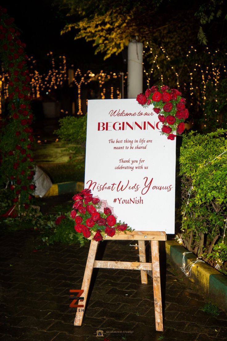 a sign with flowers on it sitting in the middle of a garden at night time