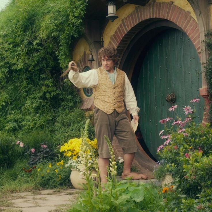 a man standing in front of a hobbot with flowers and plants around him