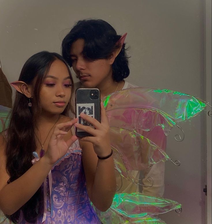 two girls dressed as tinkerbells are looking at their cell phones in the mirror