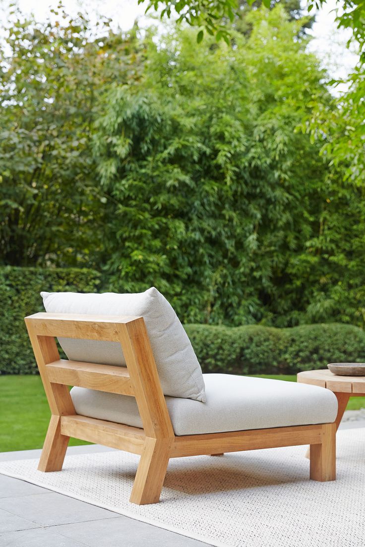 a wooden lounge chair sitting on top of a white rug next to a green bush