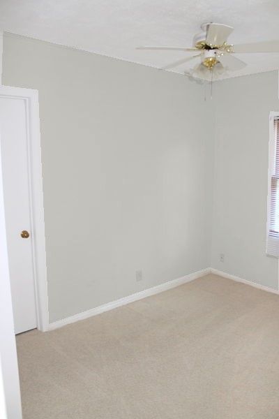 an empty room with a ceiling fan and window in the corner on the far wall