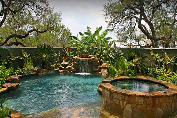 an outdoor swimming pool surrounded by trees and rocks, with a waterfall in the middle