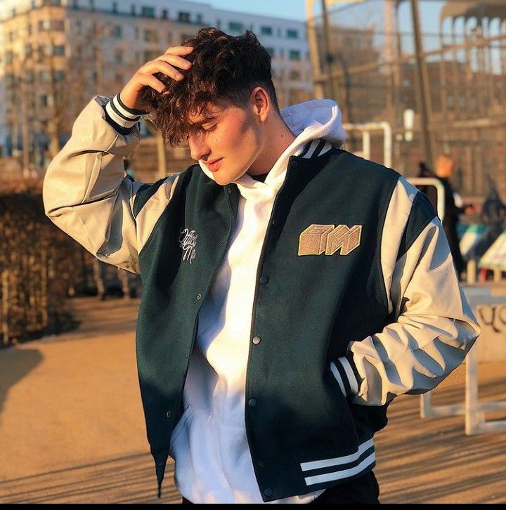 a young man wearing a green and white jacket standing in front of a building with his hands on his head