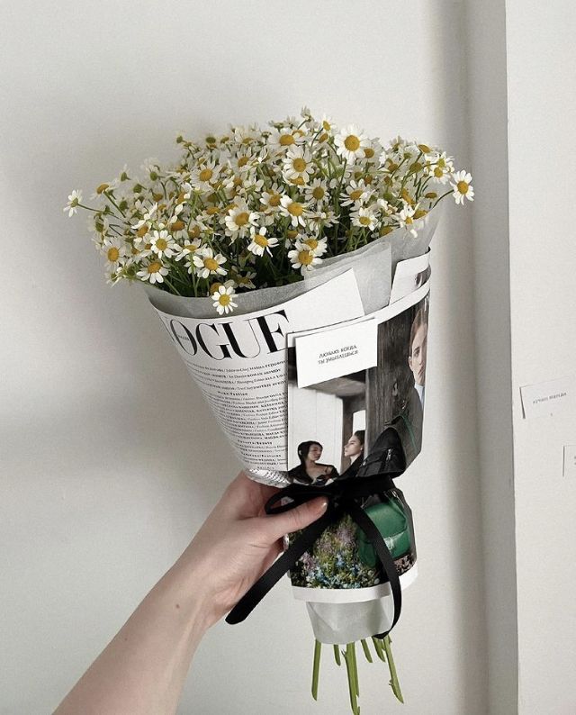 a person holding a bouquet of daisies in front of their face and magazine on the wall