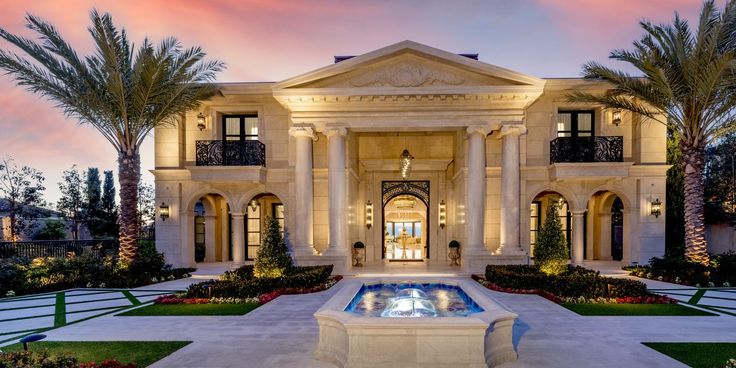 a large house with a fountain in front of it and palm trees around the entrance