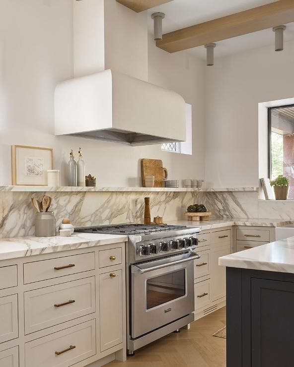 a kitchen with white cabinets and marble counter tops, an oven and stove hood in the center