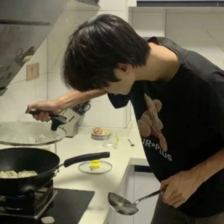 a man is bending over to look at the food he has cooked on the stove