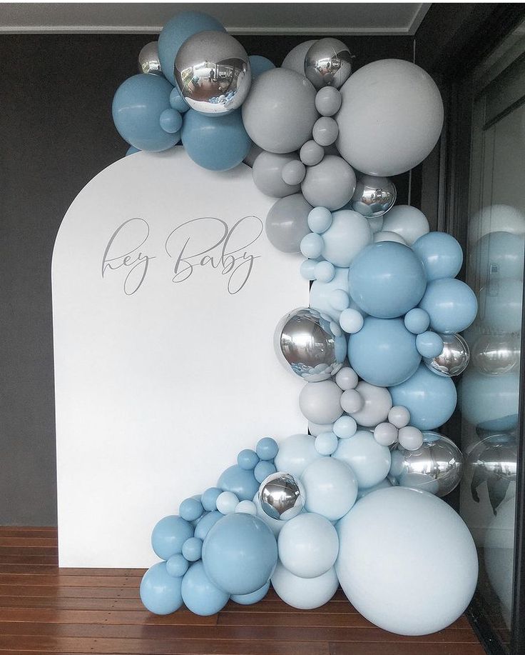 an arch made out of balloons and silver balls is displayed in front of a baby's name sign