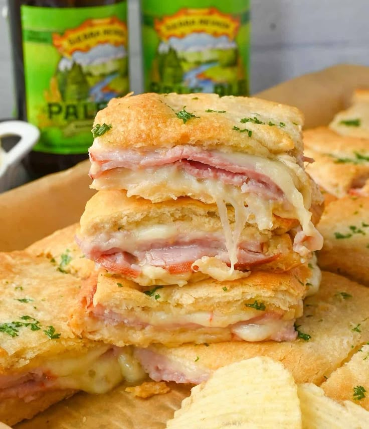 several sandwiches stacked on top of each other next to crackers and beer bottles in the background