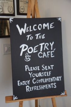 a welcome sign to the poetry and cafe in front of some framed pictures on a wall