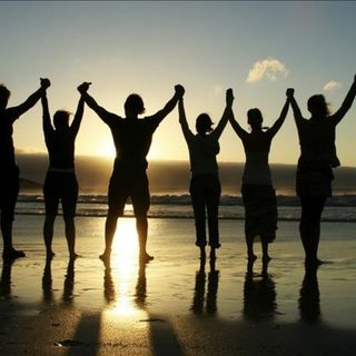 a group of people standing on top of a beach next to the ocean at sunset