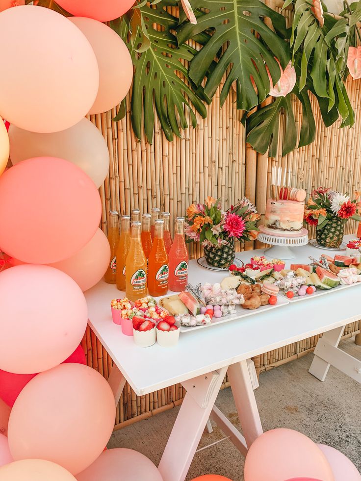 a table topped with lots of food next to a bunch of pink and orange balloons