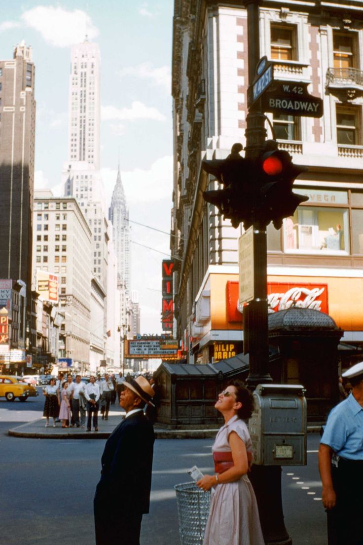 a man and woman standing on the corner of a busy street in new york city