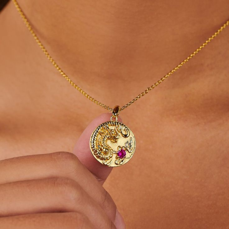 Discover the majestic allure of the Fiery Dragon Coin Pendant, a piece rich in symbolism and splendor. This ornate coin necklace showcases a meticulously carved dragon, an emblem of strength and good fortune, set against a backdrop of gleaming gold. At the heart of the design lies a vibrant ruby, a gemstone celebrated for its passion and vitality.   Hypoallergenic, nickel, and lead-free. Tarnish resistant. Made of 14K gold plated over sterling silver. H2O sensitive. Before showering or working out, remove your plated jewelry. Clean your piece by buffing gently with a dry cloth and store it in your pouch. Fiery Dragon, Carved Dragon, September Birthstone Jewelry, Forever Jewelry, Jewelry Ring Box, Pearl Jewellery Earrings, Evil Eye Jewelry, Coin Necklace, Mens Jewelry Bracelet