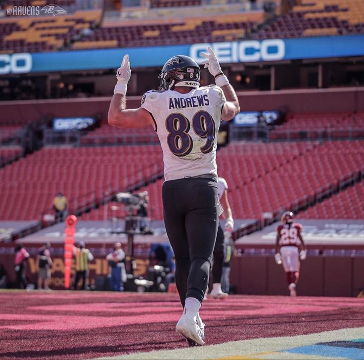 a football player running on the field with his arms in the air and one hand up