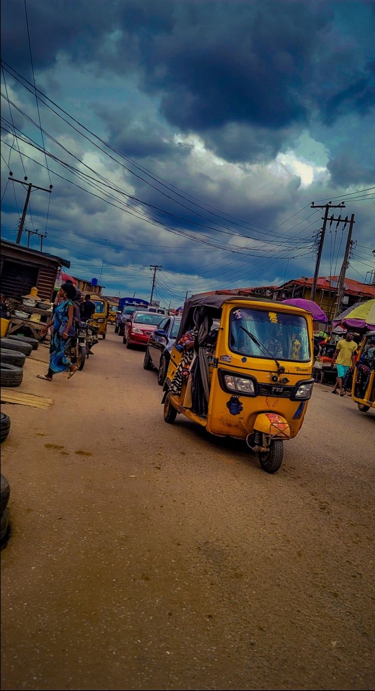 a small yellow car driving down a street next to parked cars and people on bicycles