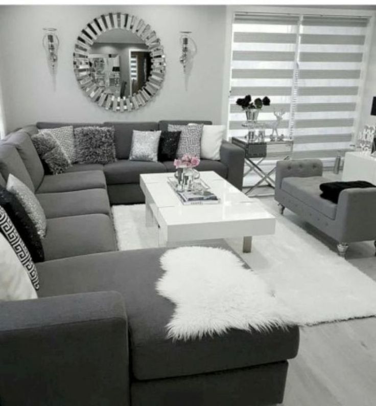 a living room filled with gray couches and white tables in front of a mirror