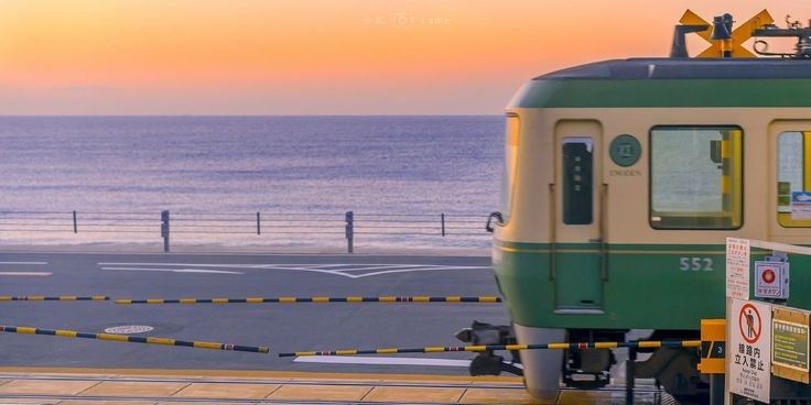 a green and yellow train on tracks next to the ocean at sunset with people standing near it