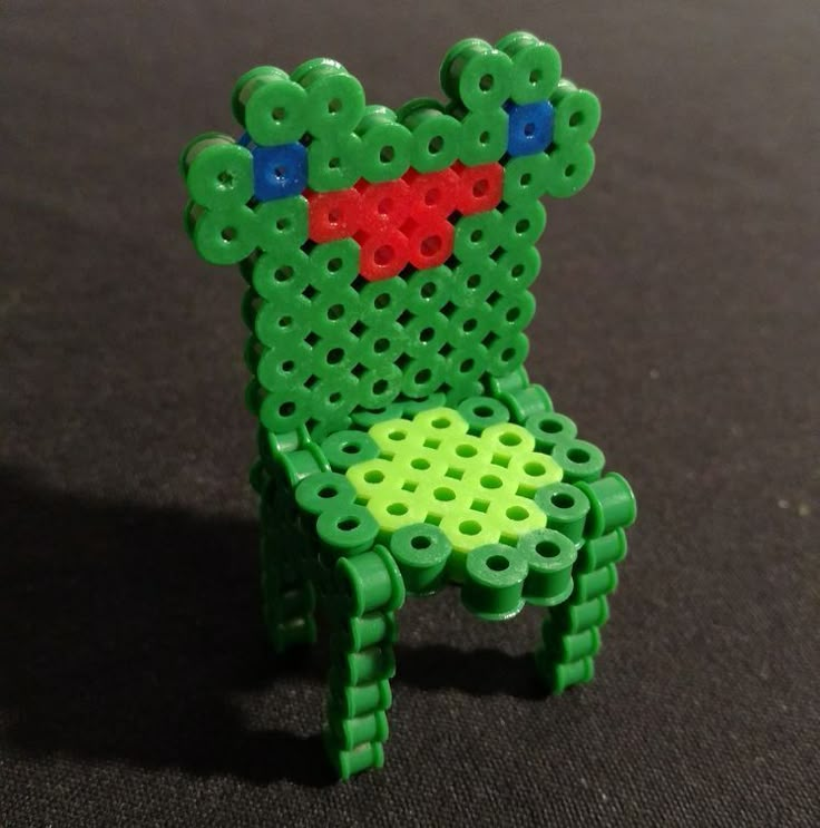 a green chair made out of legos sitting on top of a black table next to a red and blue object