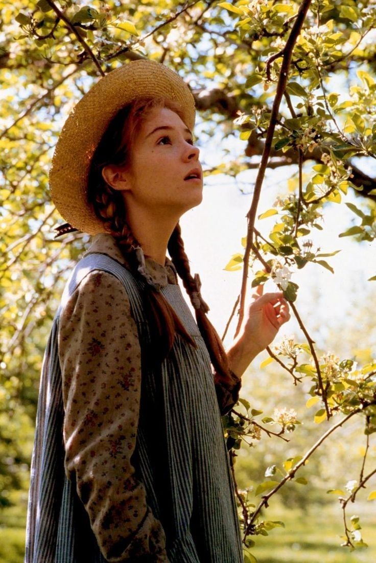 a woman wearing a hat standing under a tree