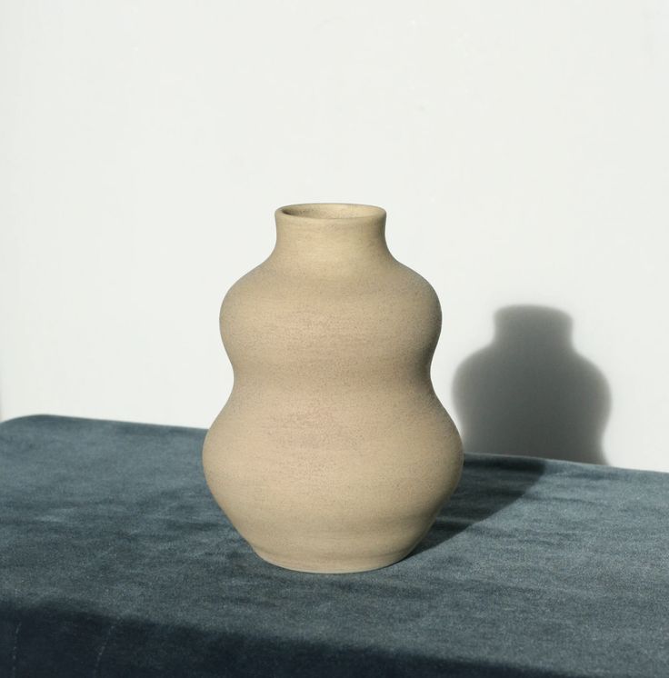 a white vase sitting on top of a blue table cloth next to a white wall