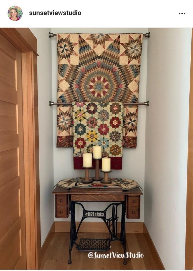 an old sewing table with two candles on it in front of a quilted wall hanging