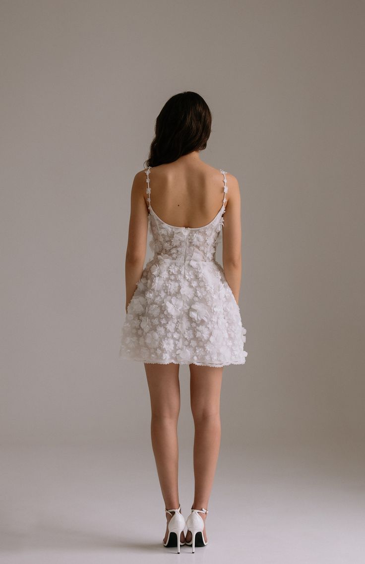 a woman in a short white dress with flowers on the skirt and heels, back view