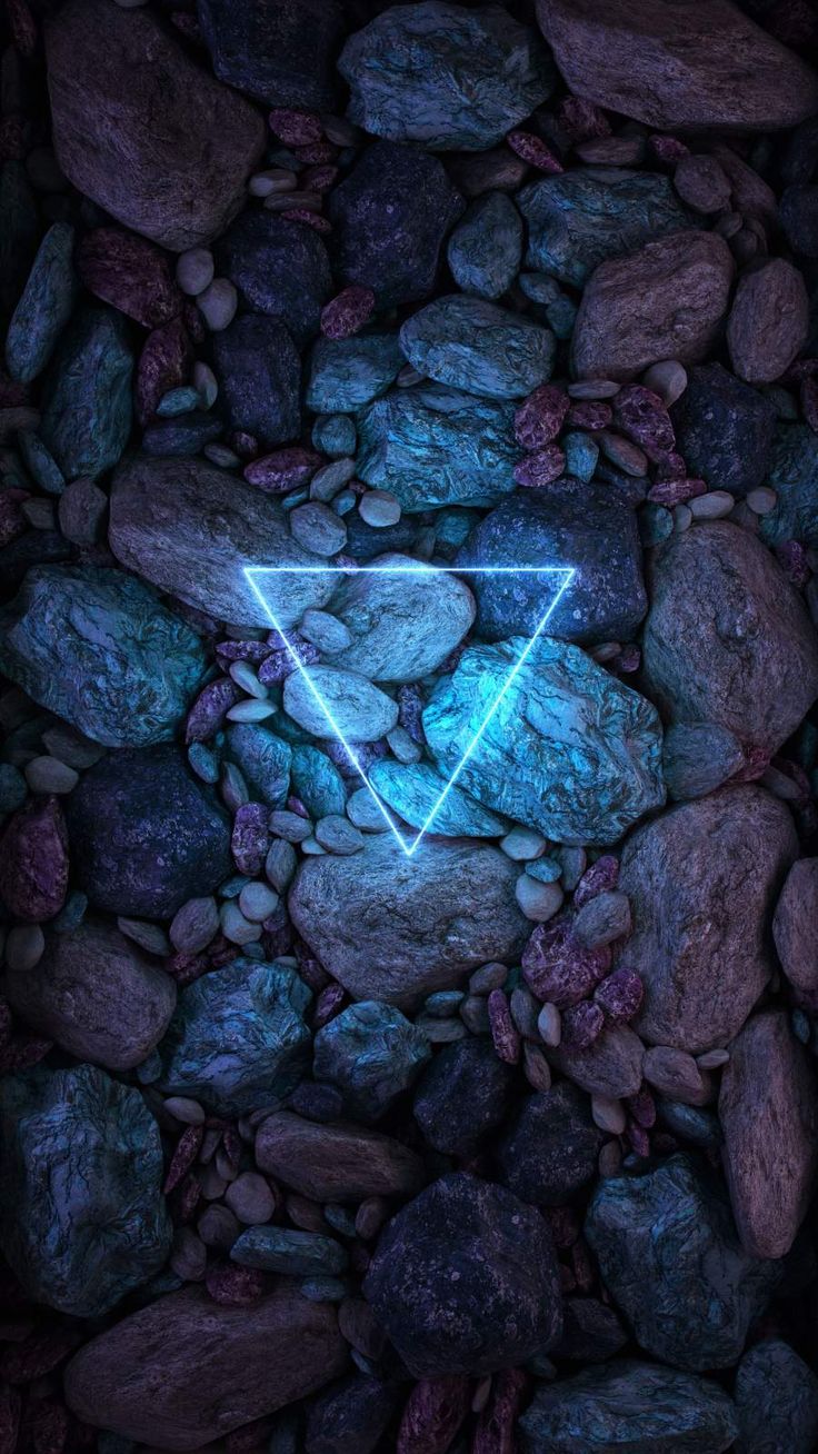 rocks and stones with a neon triangle on them in the middle of it, against a dark background