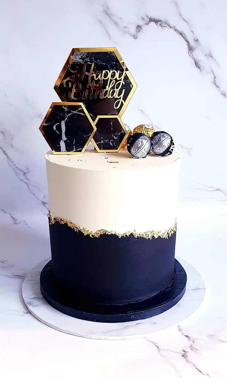 a white and black cake with gold decorations on it's top is sitting on a marble table