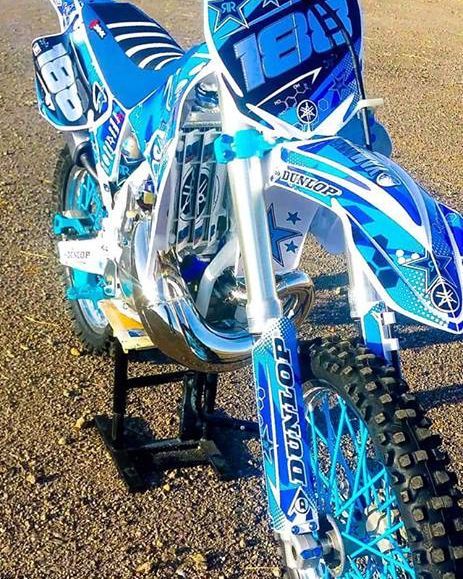 a blue and white dirt bike parked on top of a gravel road