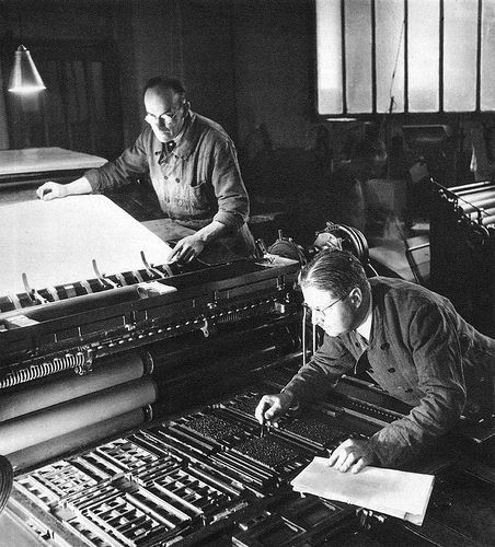 two men are working on an old typewriter in a room full of other machines