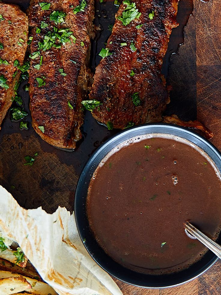 some meat and sauce on a wooden cutting board with pita bread next to it