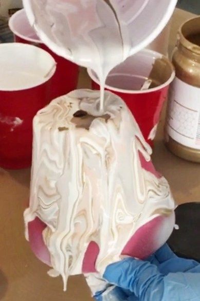 a person in blue gloves pours white frosting onto a cake on a table