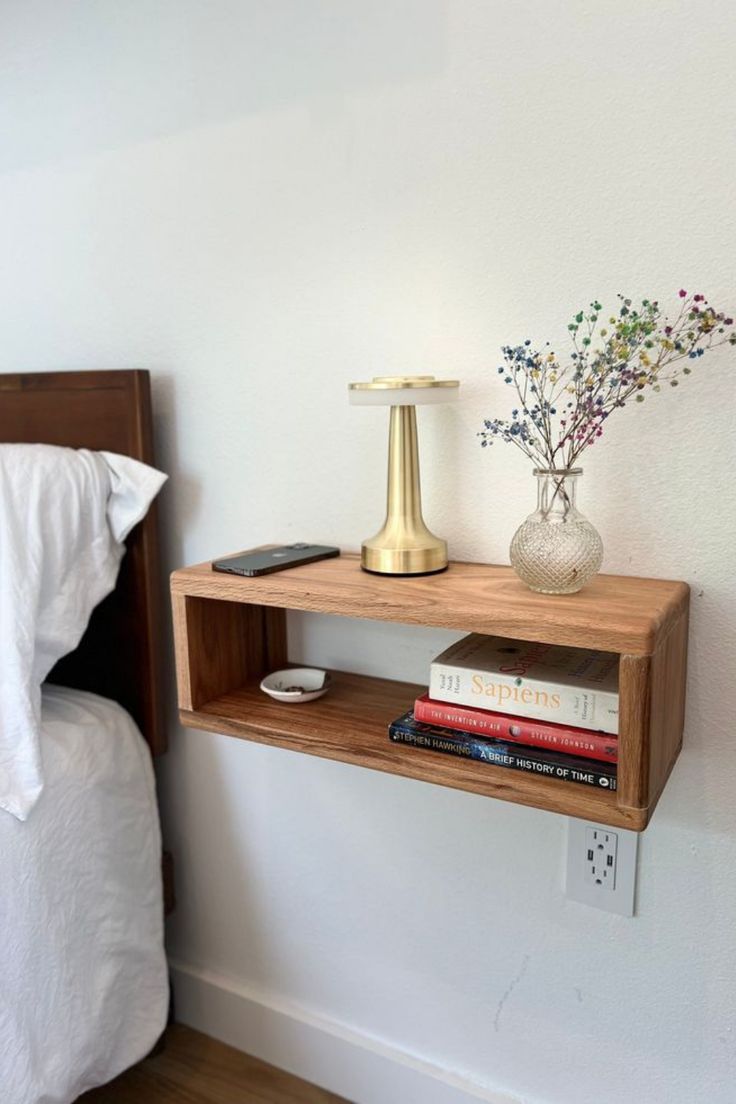 a wooden shelf with some books and a lamp on it next to a white bed