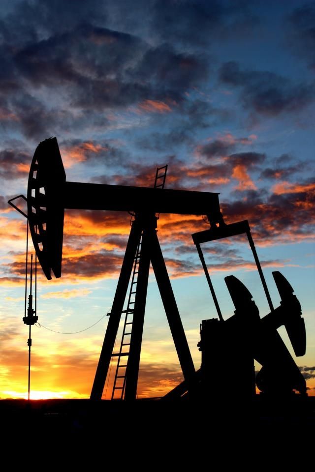 an oil pump at sunset with the sun setting in the background and clouds above it