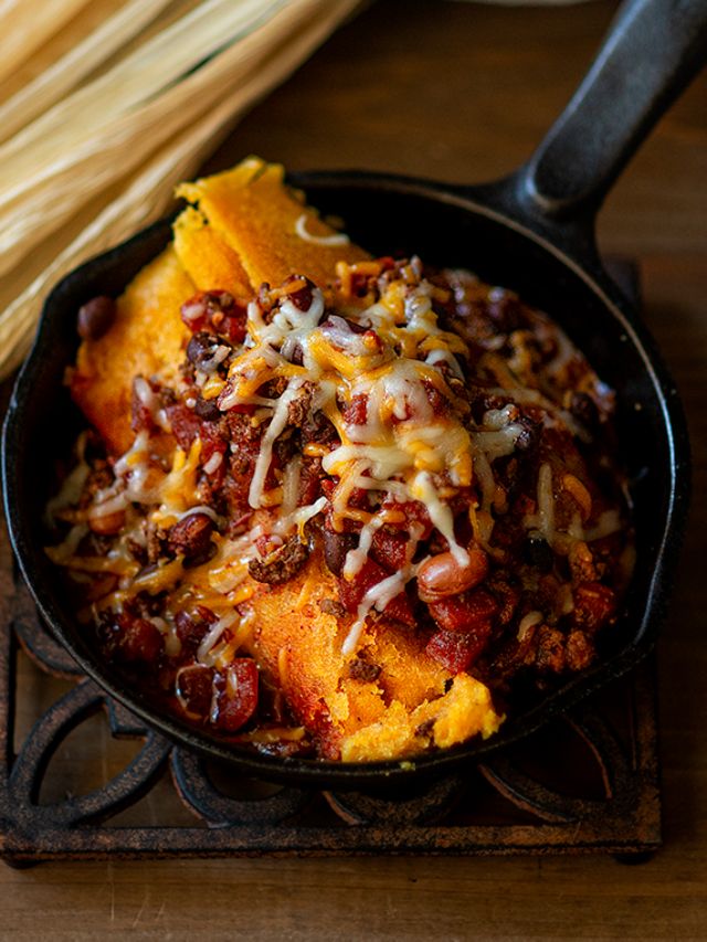 a skillet filled with chili and cheese on top of a wooden table next to corn stalks